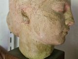 une sculpture représentant une tête, posée sur un socle en bois