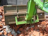 a green excavator that is on top of a pile of rubble