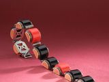 a close up of a red and black roller chain on a pink surface