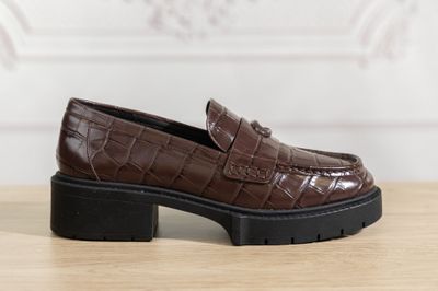 brown croced leather loafers with black soles on a wooden table