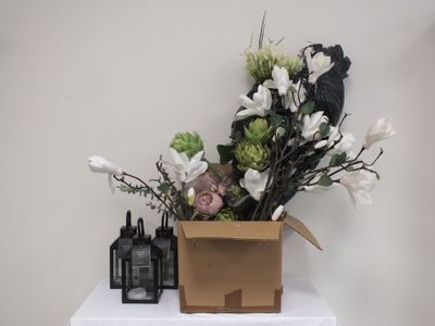 un vase de fleurs posé sur une table blanche, à côté de flacons de parfum