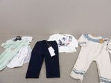 Plusieurs vêtements de bébé sont disposés sur un canapé dans une pièce.