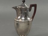 une cafetière ancienne en argent, dotée d'une poignée en bois sur un fond gris