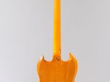 an orange electric guitar hanging from a string on a white wall