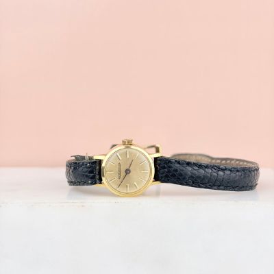 un gros plan d'une montre posée sur une surface blanche, avec un fond rose