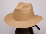 un chapeau de paille beige posé sur un porte-chapeaux en bois, devant un mur blanc