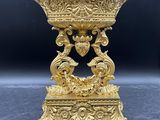 un vase en or richement décoré, posé sur un socle, sur fond noir