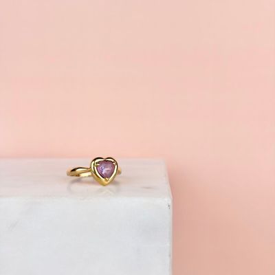 une bague en or ornée d'une pierre rose en forme de cœur posée sur un bloc de marbre