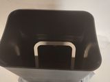 a black trash can with a metal handle on a white surface