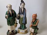 three figurines of asian people sitting on a white surface