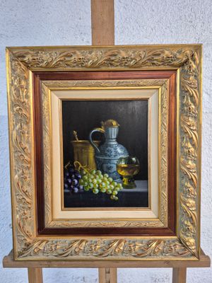 un tableau représentant des raisins et une cruche en argent posé sur un chevalet