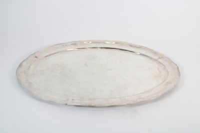an oval silver tray on a white surface with a silver handle