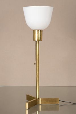lampe de table en laiton avec un abat-jour en verre blanc posé sur un socle noir
