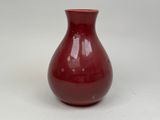 un vase rouge posé sur une surface blanche