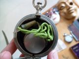 une personne tenant une montre à gousset munie d'une ficelle verte