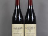 two bottles of red wine sit on a table in front of a gray background