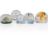 six œufs en verre ornés de motifs variés, posés sur une surface blanche