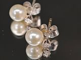 une paire de boucles d'oreilles en perles et diamants posées sur un fond noir