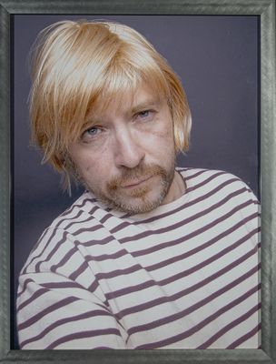 une photo d'un homme aux cheveux blonds portant une chemise rayée