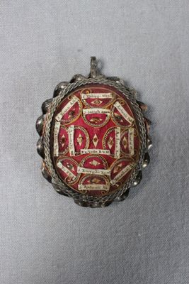 une photo d'une broche rouge et dorée posée sur un tissu blanc