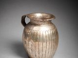 un vieux vase en argent posé sur une table blanche