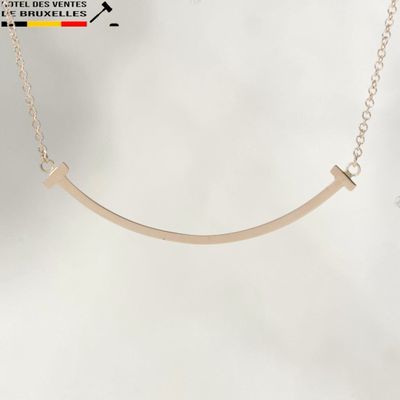 a close up of a gold necklace with a curved bar on a chain