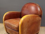 une image représentant un fauteuil en cuir marron posé sur un parquet en bois massif