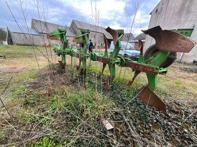 une charrue verte posée dans l'herbe à côté d'un bâtiment