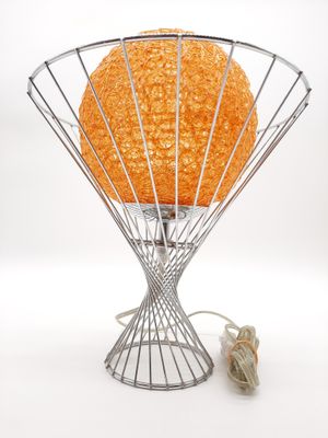 une lampe orange posée sur un pied en fil de fer