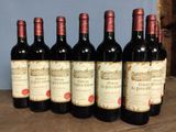 six bottles of red wine are lined up on a wooden table