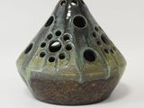 un vase vert percé de trous posé sur une surface blanche