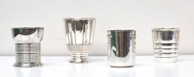 quatre vases en argent sont alignés sur une surface blanche