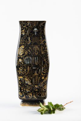un vase noir et doré posé à côté d'une feuille verte