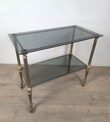 Une desserte à roulettes, en métal doré, plateaux de verre, …