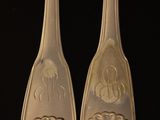 two silver spoons with designs on them sitting on a black surface