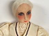 a doll with white hair and a red belt sitting on a table
