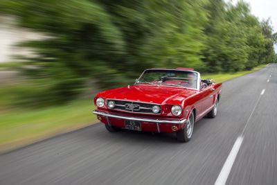 a red car driving down the road with trees in the background