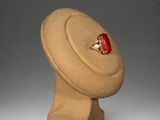 beige hat with a red ring on top of it on a stand