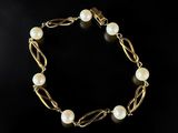 a gold bracelet with pearls on a black background