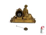 a gold clock with a woman sitting on it