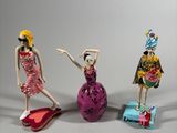 three figurines of women in dresses and hats are posed in front of a gray background