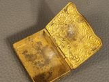 a gold plated box with a small square inside on a leather surface