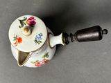 a small white tea pot with a flowered design on it