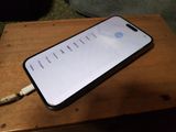 Un iPhone est posé sur une table en bois, avec un chargeur branché dessus.