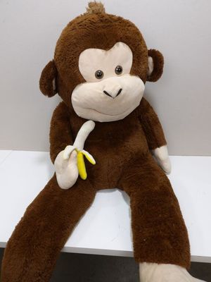 un singe en peluche assis sur une étagère, une banane dans la main