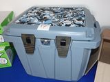 une glacière bleue posée sur un tapis bleu à côté d'une boîte