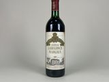 une bouteille de vin rouge posée sur une table blanche, sur fond gris
