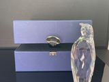 un flacon de parfum en verre transparent posé sur une table, à côté d'une boîte violette