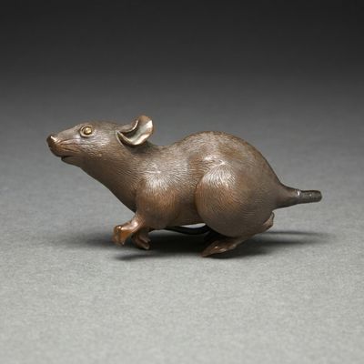 bronze figurine of a mouse with horns on a gray surface