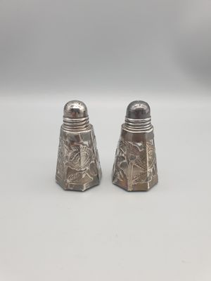 deux salières et poivrières en argent posées sur une surface blanche